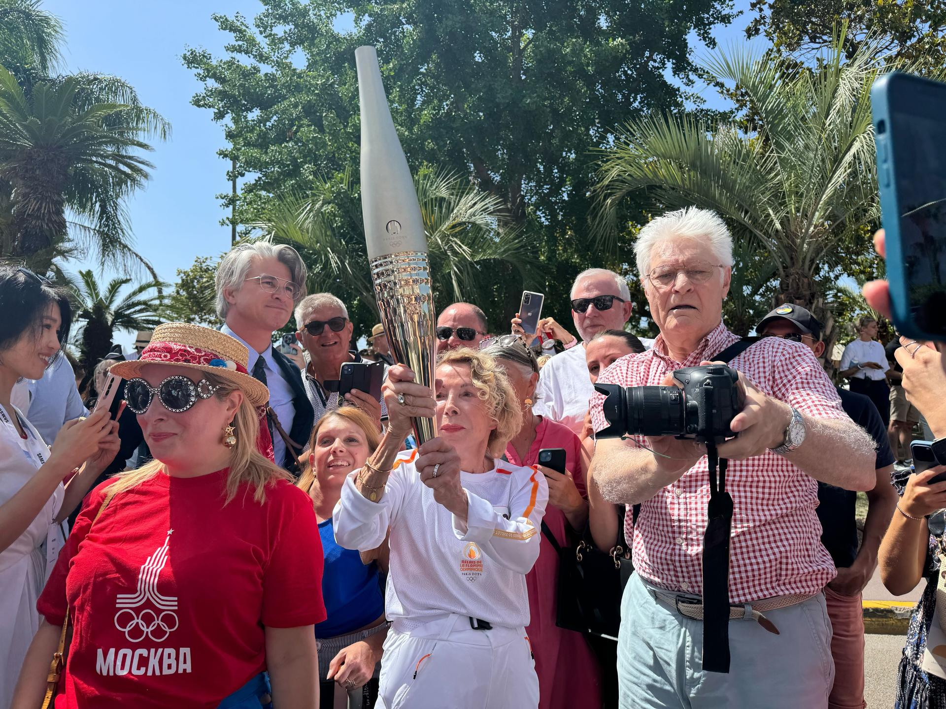 Group of people and photographers surround a woman holding the Olympic torch.
