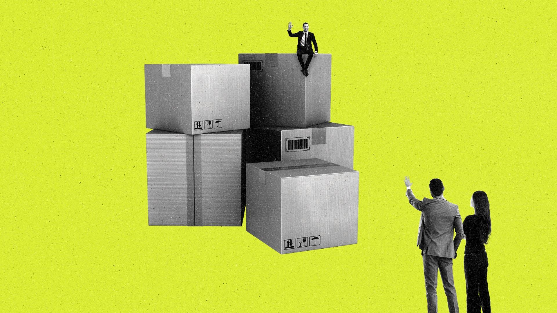 Miniature man sitting on cardboard boxes waves to a couple nearby.