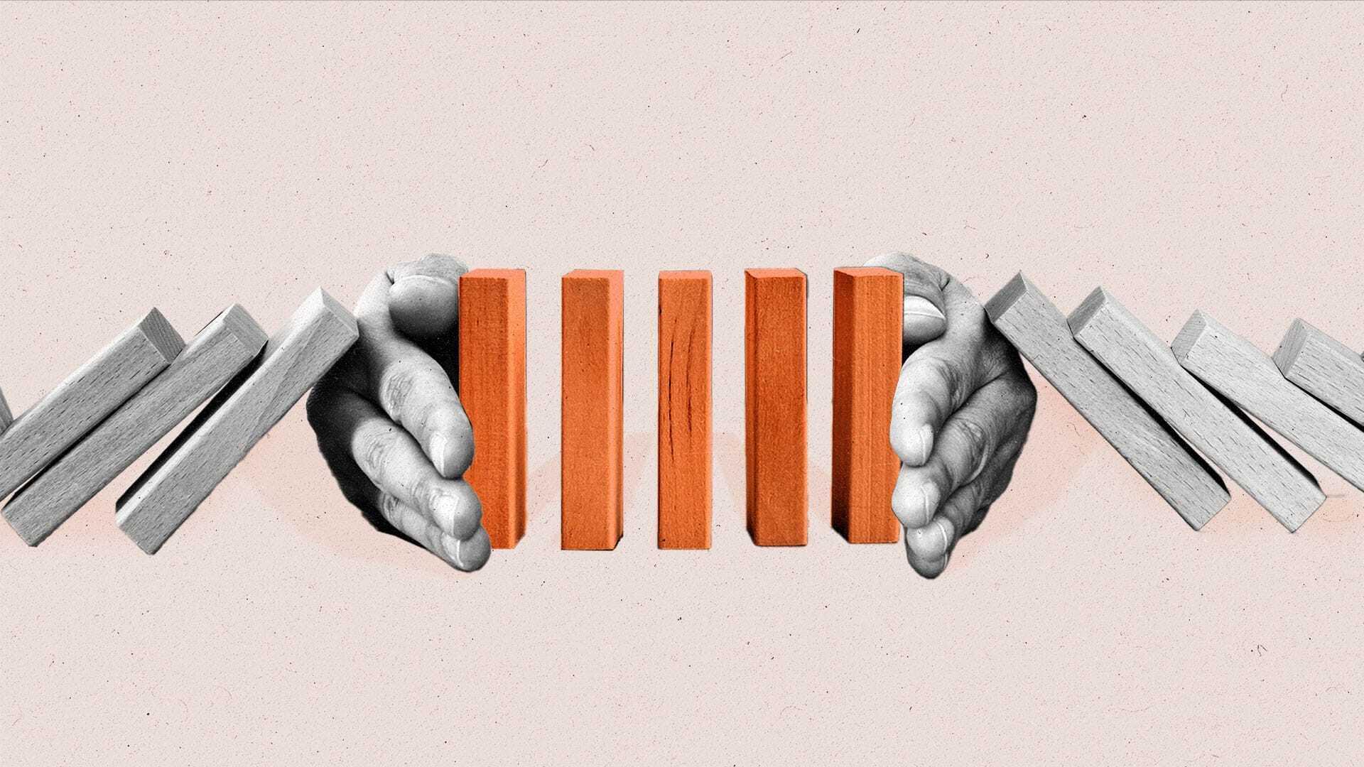 Two hands protect 4 upright blocks from a falling domino effect.