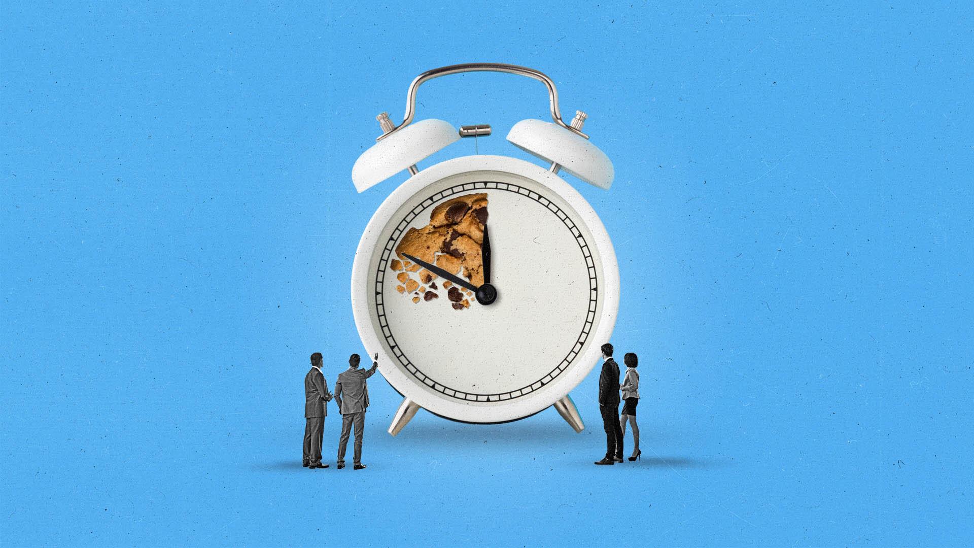 Three men watch an alarm clock that features a section made of a crumbling cookie.