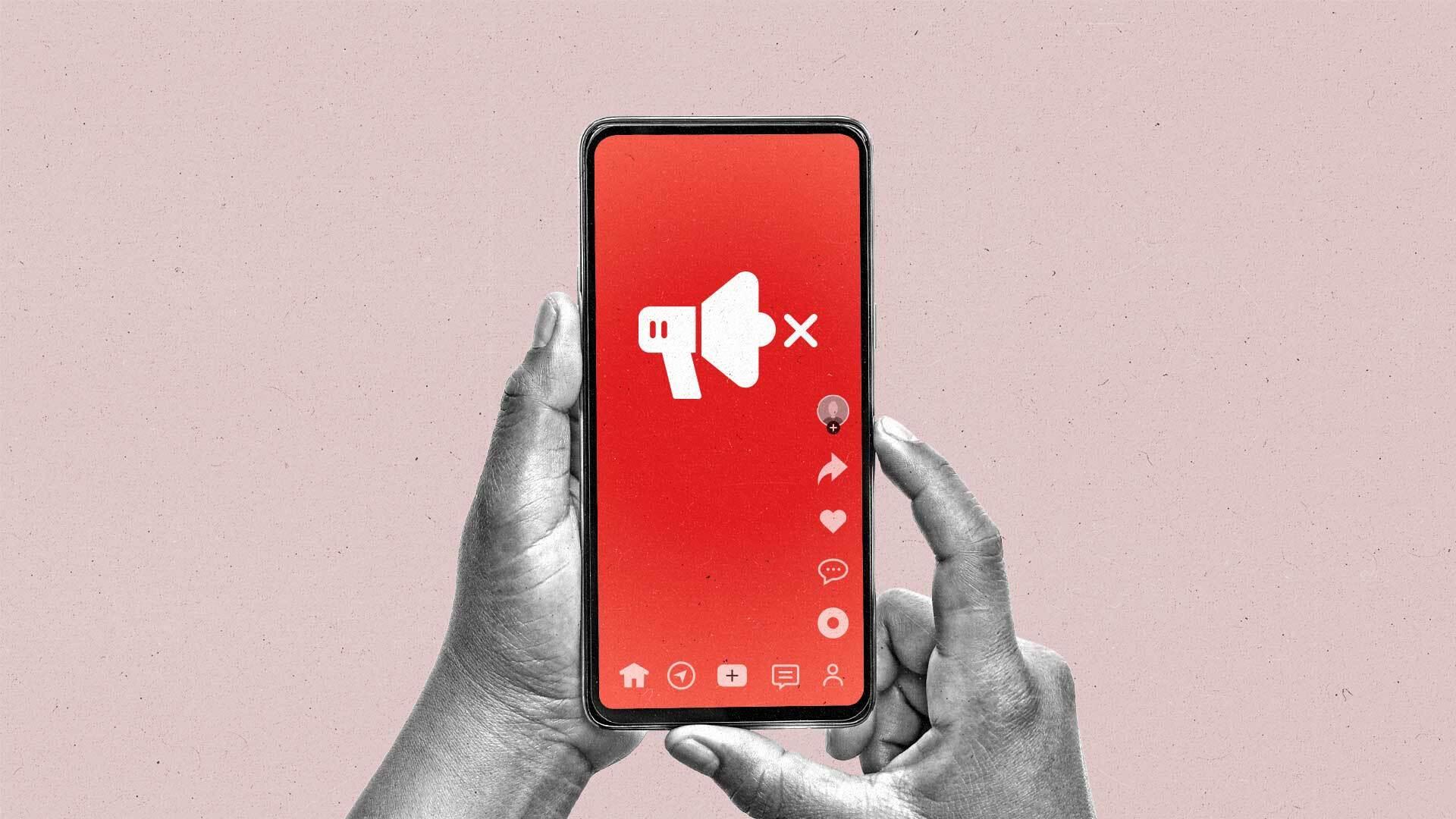 Two hands hold a smartphone showing a social media site with a megaphone icon and an X next to it.